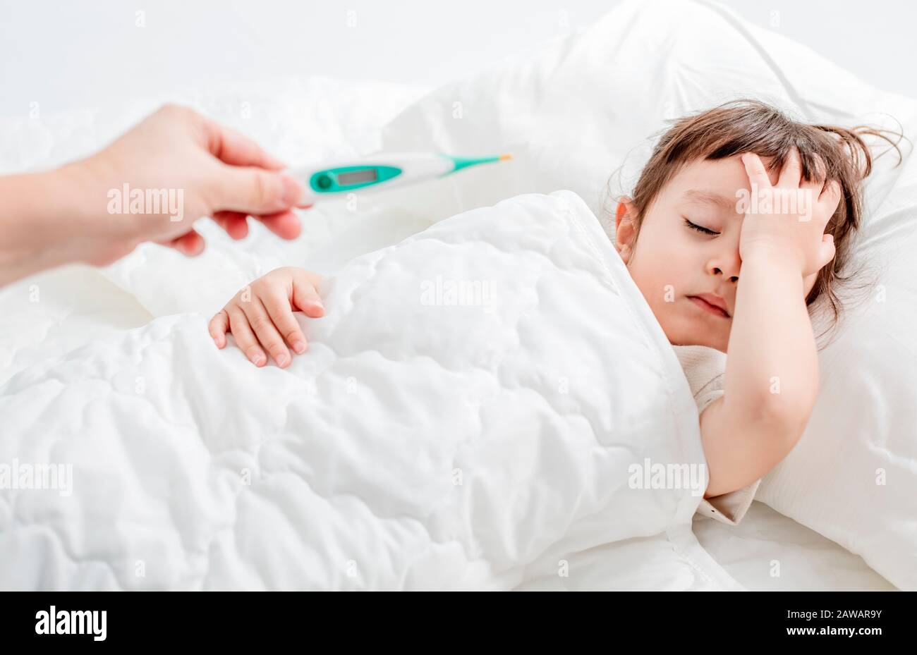 Sick child with flu fever laying in bed and mother holding thermometer Stock Photo